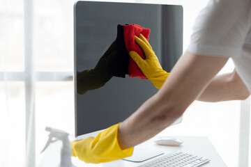 Person cleaning room, cleaning worker is using cloth to wipe computer screen in company office...