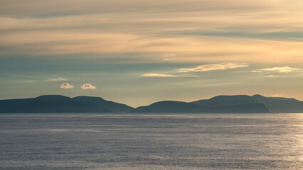 Fototapeta premium View over blue green oceanic water and distant islands at sunset colors as background with copy space. Concept holidaying and travel at sea.