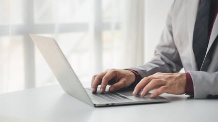 Person typing on laptop keyboard, businessman working on laptop, he is typing messages to colleagues and making financial information sheet to sum up the meeting.