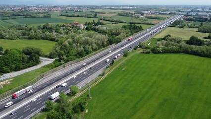Aerial view of A4 freeway in Cavenago di Brianza, Po Valley near Milan, Lombardy, Italy. Italian landscape with industrial buildings, towns and highway traffic seen from drone flying in the sky