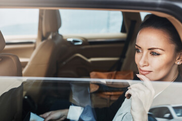 Looking out at the busy streets. a confident young businesswoman seated in a car as a passenger while busy on her phone and looking out of the window.