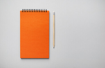 Blank orange notebook and pencil on gray paper background. Template for branding design. Flat lay.