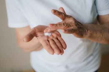 Hands of old elderly applying lotion on hands, rubbing her palm with thumbs cream. Prevent dryness, nourishing dry skin and care for sensitive skin.