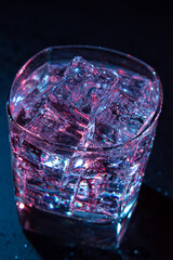 Glass of cold water with ice with colored lighting on a black background. refreshing drink