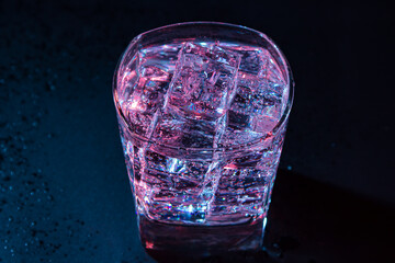 Glass of cold water with ice with colored lighting on a black background. refreshing drink