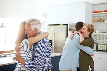 You can never have too many hugs. a loving family greeting each other with hugs in the kitchen at home.