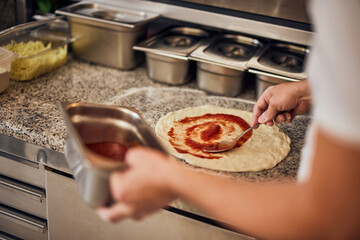 Chef baker making pizza in the kitchen, adding tomato sauce to pizza dough.