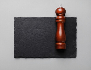 Photo of pepper mill and slate plate on gray paper background. Copy space. Flat lay. © Veresovich
