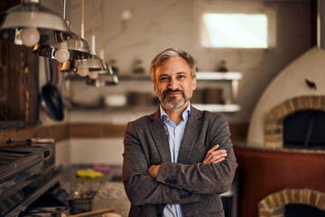 Portrait of a successful male owner of a pizzeria, standing in the kitchen.