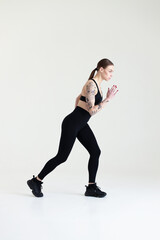 A young girl with brown hair, with a tattoo in a black top and leggings on a white background. Sports, fitness, starts running