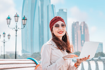 From the comfort of her laptop, a freelancer or student indian girl immerses herself in the vibrant and dynamic atmosphere of downtown Abu Dhabi, fueled by the energy of the bustling city.