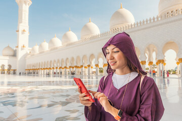 The modern and the ancient come together as a tourist girl using wi-fi mobile internet on her phone inside the Sheikh Zayed Grand Mosque.