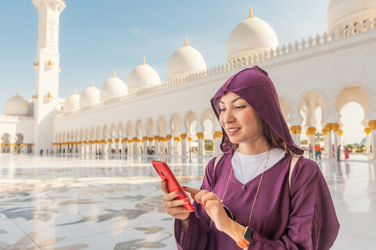 The modern and the ancient come together as a tourist girl using wi-fi mobile internet on her phone inside the Sheikh Zayed Grand Mosque.
