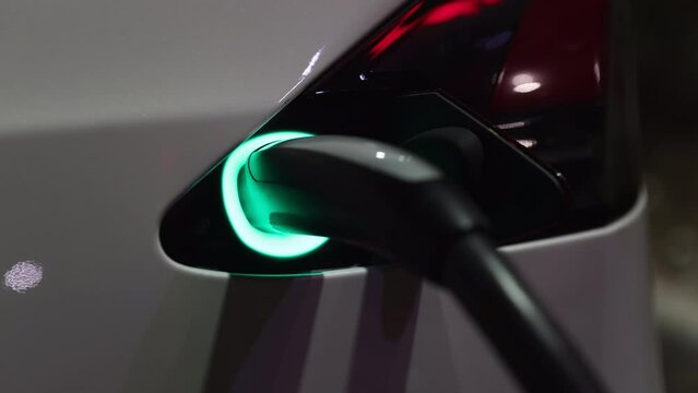 Electric car charging at night - close up on charge port flashing green