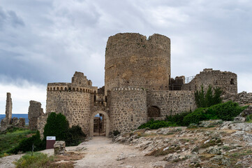 Fototapeta na wymiar imagen del castillo de Moya, castillo de piedra entre naturaleza, suelo de rocas y tierra con hierbas verdes y el cielo nublado 
