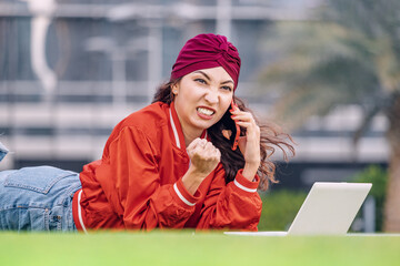 Frustrated and angry indian woman talk by phone and working outdoor on her laptop pc