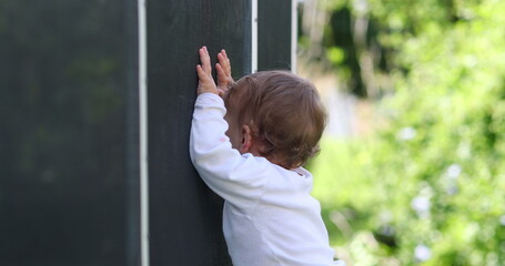 Baby standing outside leaning on pool fence