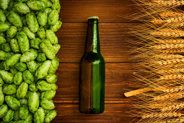 A bottle of beer on a wooden background with green hops and wheat ears