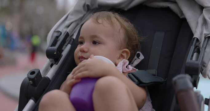 Young baby girl sits in stroller holding onto water sippy cup - close up