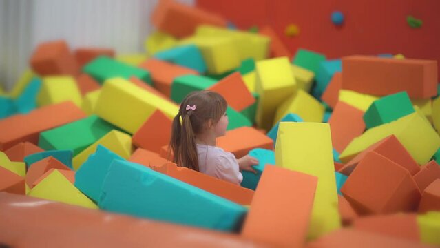 Little happy girl play and have fun in a dry pool with soft multicolored cubes in a children's entertainment center and throw paralon block in the playroom.
