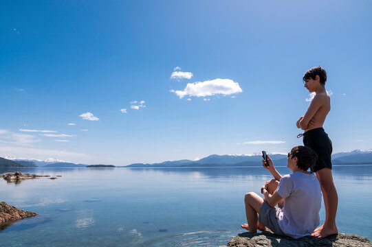 Dos hermanos hablando por video chat con el celular desde la inmensidad  de la naturaleza en medio del lago y las montañas. 