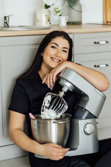 A woman cook sits on the floor and holds a professional mixer next to her