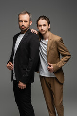 well dressed dad and teenage son in suits standing together isolated on grey.