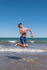 Boy happily enjoying the sea on his summer vacation, doing big jumps on the shore of the beach.