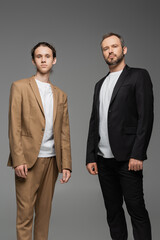 well dressed teenage boy and dad in suits looking at camera isolated on grey.