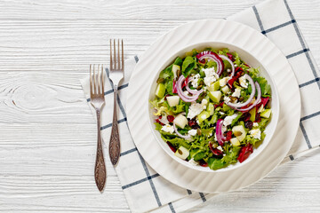 Green Salad with Apples, Goat Cheese, Cranberries, Red Onion and green pumpkin seeds in white bowl on white wood table with forks, horizontal view from above, flat lay, free space