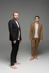 full length of well dressed father and teenage son in suits standing together on grey.