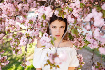 Young Gilrs Face Looking at the Camera, Standing in the Sakura Flowers Blooming. Beauty Portrait. Femininity and Natural Beauty Concept