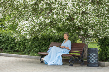 Fototapeta premium Portrait of a middle-aged woman in a blue dress sits on a bench