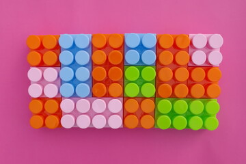 Many toy blocks in different pastel colors making up one large square shape in top view. Toys and games. Isolated on pink background