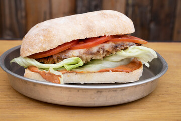Plant based vegetarian food. Closeup view of a sandwich with notmeat, lettuce, mozzarella cheese and tomato in a metal dish with a wooden background.