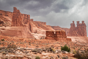 Red sandstone rock formations and the Three Gossips in Arches National Park with dark storm clouds in the arid desert landscape environment.