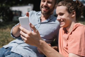bearded father and happy teenage son smiling while looking at smartphone.