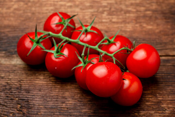 Branch of fresh cherry tomatoes on a brown wooden background.