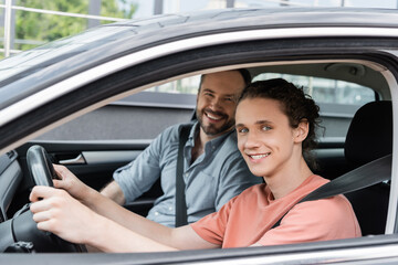 cheerful father and teenage son looking at camera while sitting together in car.