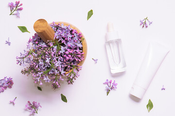 Fototapeta na wymiar Wooden mortar with fresh lilac flowers and two white cosmetic tubes on white background top view. Natural herbal cosmetic banner.
