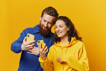 Man and woman couple smiling merrily with phone in hand social media viewing photos and videos, on yellow background, symbols signs and hand gestures, family freelancers.