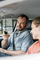 cheerful and bearded man holding car key next to son in modern auto.