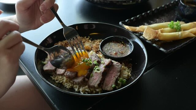 beef fat garlic ​fried rice with​ ​beef steak ​and topping with pickled egg yolk in a bowl on wooden table. Grilled Meats, thai is menu is fusion food.