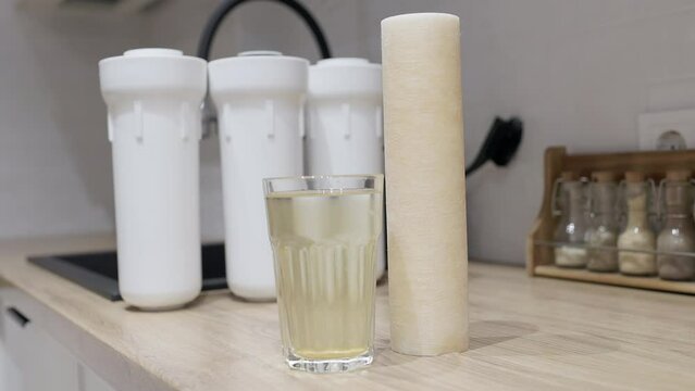 Used water filter cartridge and glass of rusty water on wooden table at kitchen. Plastic set with three filter cartridges reverse osmosis water purification system to drinkable condition.