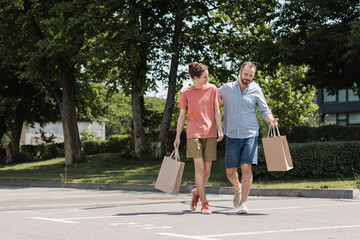 Obraz premium bearded dad and happy teenage son walking with shopping bags outdoors.