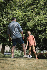 happy teenage boy playing soccer with his father in green summer park.