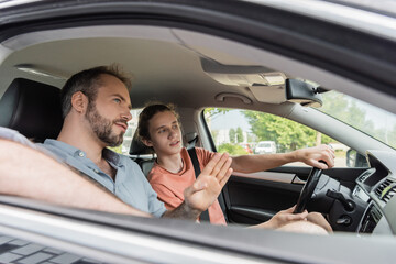 bearded dad pointing while showing direction to teenage son driving car.