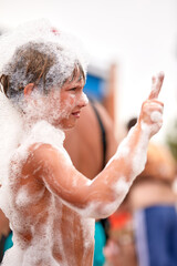 Happy little boy with foam on his head having fun in a water park, in wet swimwear at a foam party or holiday on a sunny hot summer day