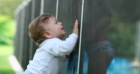 Cute baby standing by swimming pool fence protection. Toddler interacting with child