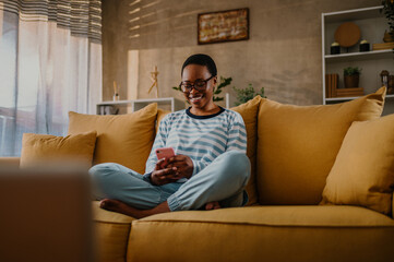 African american woman using a smartphone while sitting on a yellow sofa at home